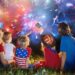 American family celebrating Independence Day. Picnic and fireworks on 4th of July in America. USA flag. Parents and kids celebrate US holiday. Children watching firework.